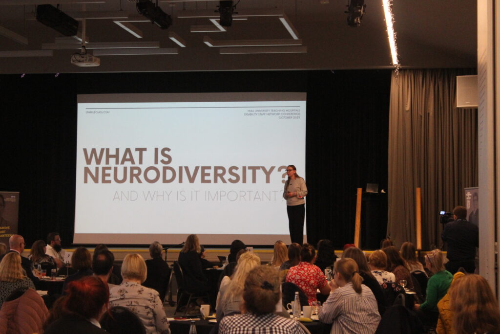 Me at a training session, it says "What is neurodiversity and why is it important?" and I'm standing on the stage.